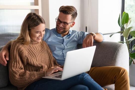 Paar sitzt auf der Couch und unterhält sich über Inhalte auf dem Laptop