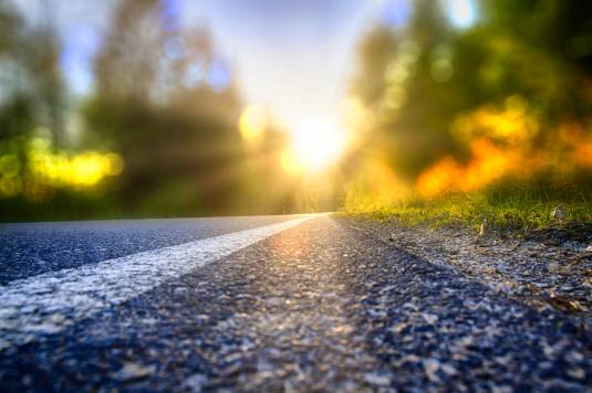 Nahansicht einer Asphaltstraße mit Sonne und Wald unscharf im Hintergrund